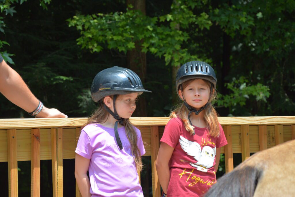 Two children wearing black helmets for horseback riding